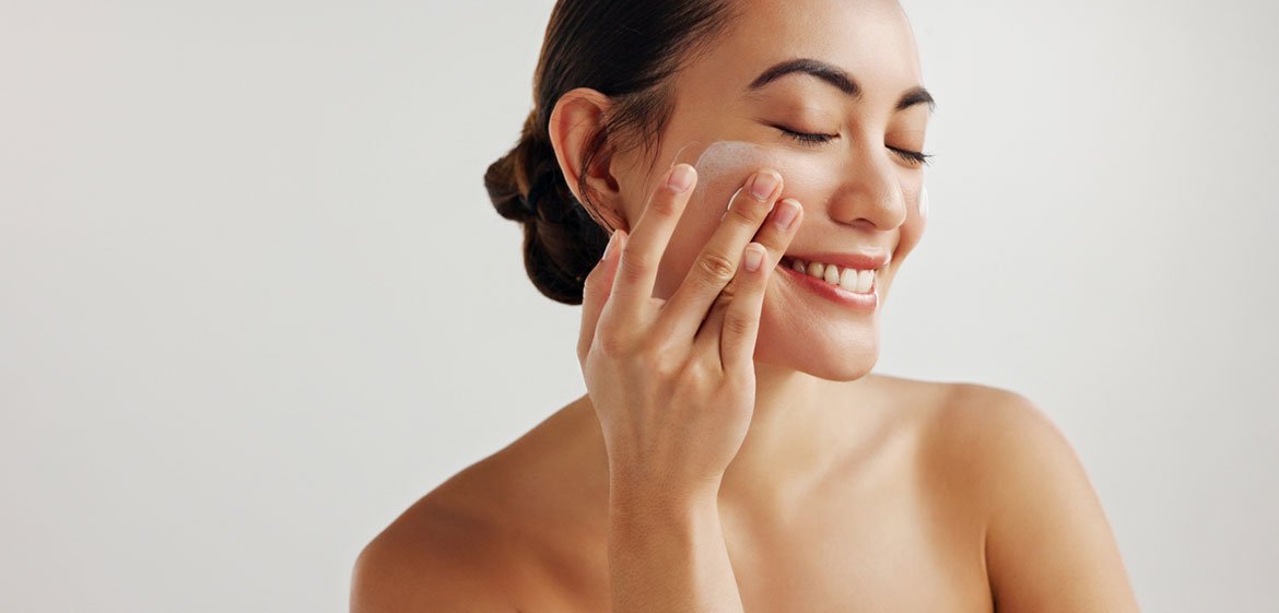 Lächelnde Frau trägt mit den Fingern eine Anti-Aging-Creme gegen Falten auf